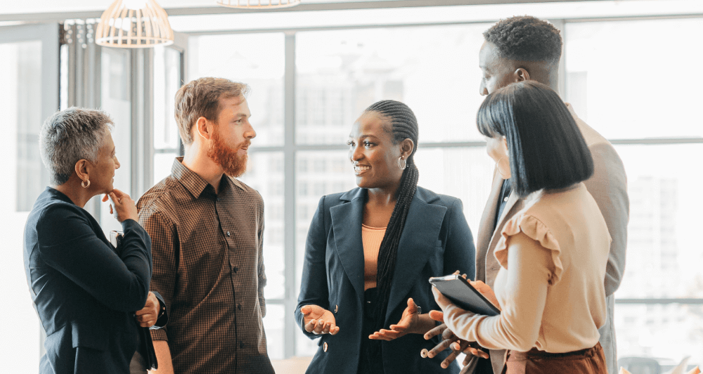 Several colleagues standing in an office setting discussing work.